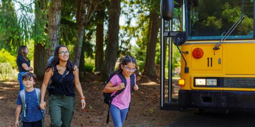 A parent picking up their kids from the school bus in a rural environment